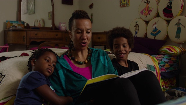 妈妈在家里的卧室里给儿子和女儿读书视频素材