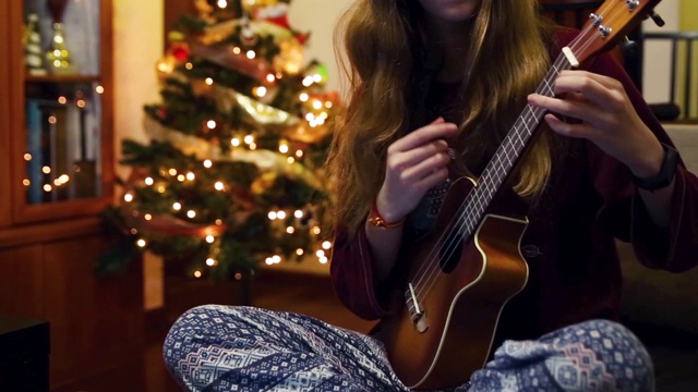 一个十几岁的女孩在圣诞树旁弹奏尤克里里琴视频下载