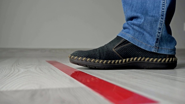 靠近孤立的鞋子和一个人的腿在地板上的红色条，等待和保持距离，而站在排队。在covid-19视频下载
