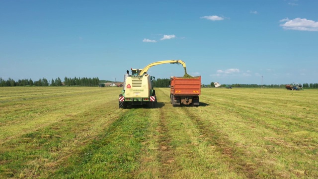 收割机收集割下的草，并把它倒进拖拉机拖车空中跟随视频素材