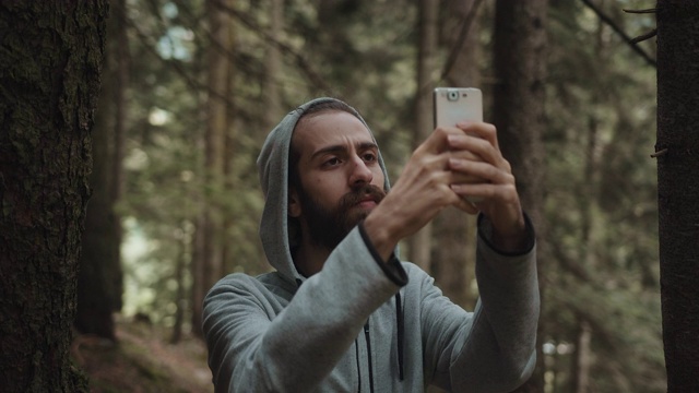 一个嬉皮士少年在森林里用手拿着手机发短信会破坏信号，这是一个有信号问题的年轻人倍感压力的问题视频素材