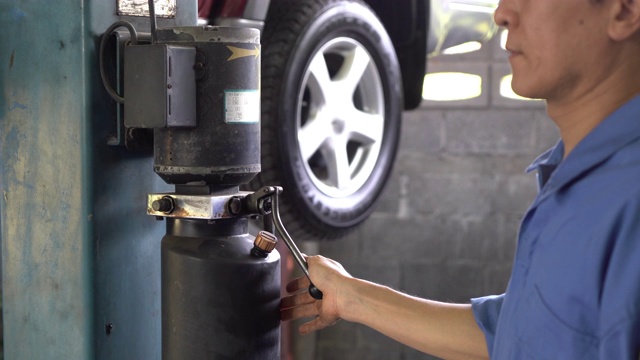 汽车修理工检查一辆被吊起的汽车的SUV悬挂的滑动镜头。在汽车修理厂工作的有经验的汽车维修技师。修理工在他的车间修理汽车视频素材