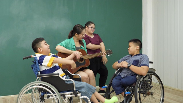 老师在教室里弹吉他陪着残疾儿童，非常开心视频下载