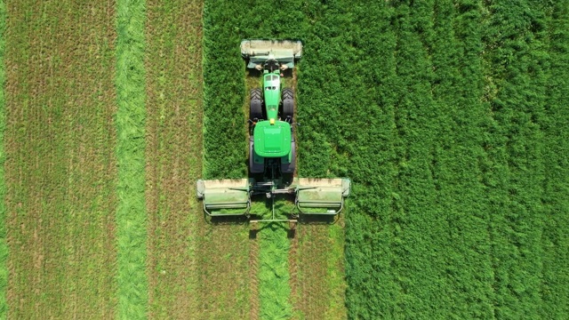 农村拖拉机为干草或牲畜饲料割新鲜的绿草空中顶部视频下载
