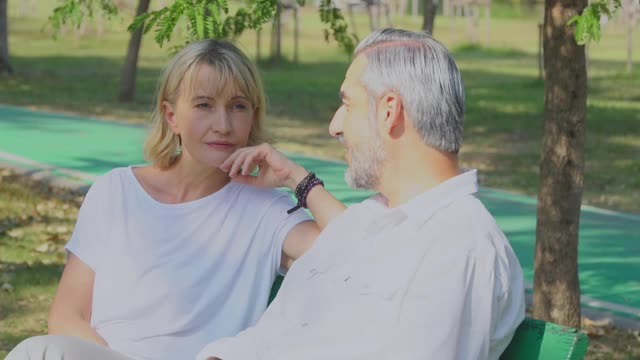 一对白人老夫妇坐在公园的长椅上聊天。退休人员周末简单的生活和生活方式视频素材