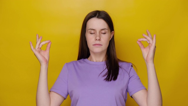 专注的年轻女性冥想与手相，平静的女孩练习瑜伽闭上眼睛，控制情绪，深呼吸，孤立在黄色的工作室背景。无压力的概念视频下载