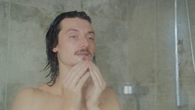 英俊的年轻长头发男子洗脸和洗澡在家里视频下载