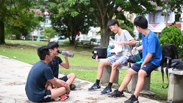 一群十几岁的亚洲华人男孩在放学后在篮球场上打篮球和练习篮球后休息和休息视频下载