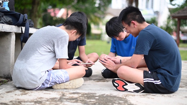 一群十几岁的亚洲华人男孩放学后在篮球场上用手机玩手机游戏z一代视频素材