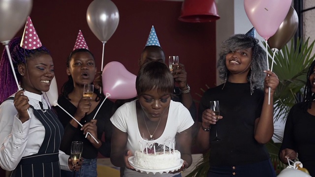 快乐迷人的非洲女孩吹蜡烛在生日蛋糕包围她的朋友视频素材