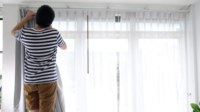 亚洲男孩在家里用窗户挂窗帘，搬家的概念。视频下载