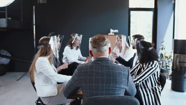 2019冠状病毒病期间的办公室安全措施。后视图男老板和各类团队在商务会议桌上戴面罩视频素材