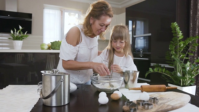 小女孩在厨房里帮妈妈用勺子搅拌做蛋糕的原料。可爱的小女孩在厨房里帮妈妈搅拌面团，把饼干放进碗里视频素材