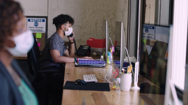 在办公室里使用电脑工作的女性和年轻人保持社交距离，并戴上口罩视频下载