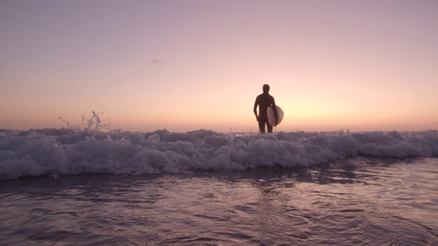 日落时分，一个年轻人带着冲浪板散步视频素材