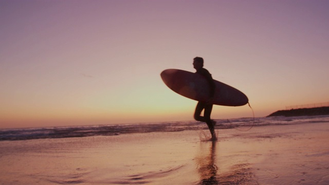 一个年轻人在日落时沿着海滩散步视频素材