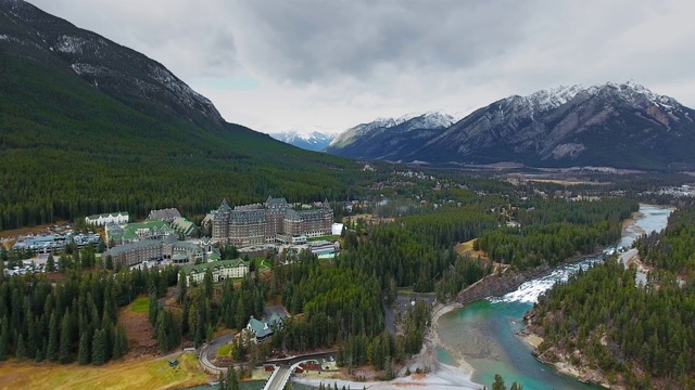 无人机摄像头捕捉到了围绕在弓河岸边的一家巨大酒店周围的美丽自然景观(班夫，阿尔伯塔，加拿大)视频素材