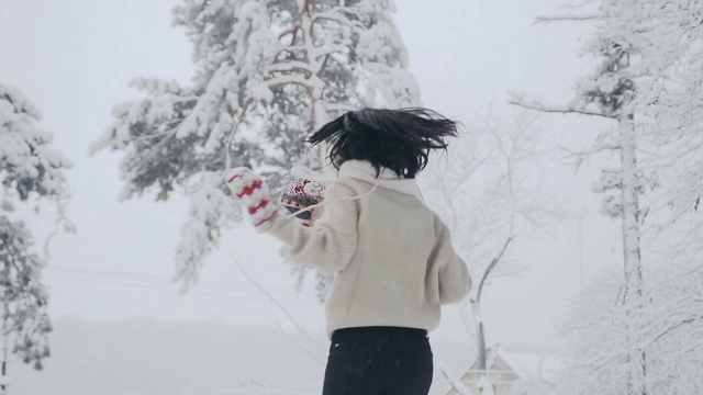 美丽的女人穿着暖和的毛衣和围巾，用连指手套遮住她的眼睛，在大自然中享受雪天视频素材