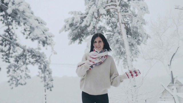 一个年轻的黑发女人的特写镜头在一个霜冻的冬天，谁走在白雪覆盖的森林在时尚的羊毛衫，温暖的围巾和针织手套视频素材