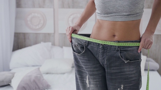 一个运动身材的女人在减肥后测量她的裤子尺寸。美丽的身体和平坦的腹部视频素材