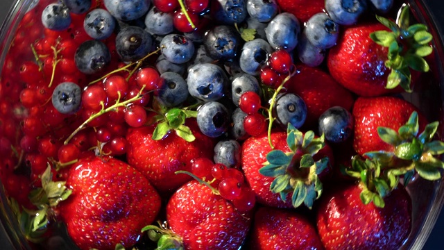 4 k。各种五颜六色的浆果在玻璃上吹旋转在黑色的背景上，草莓，覆盆子，黑莓，蓝莓，健康的食品概念。视频下载