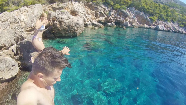 无忧无虑的年轻夫妇跳入克罗地亚亚得里亚海阳光明媚的海洋视频素材