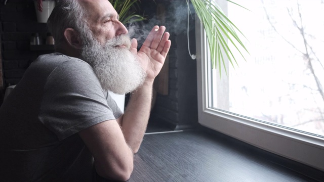 一位留着胡子、头发花白的老人望着窗外，然后在厨房里抽烟视频下载