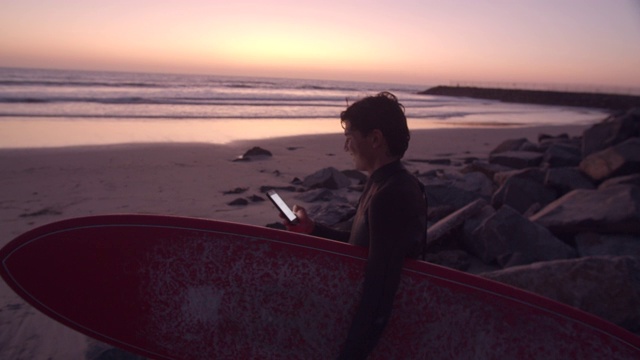 一个年轻人冲浪后在海滩上用手机视频下载