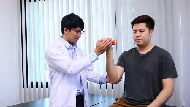 亚洲年轻男性理疗师，在诊所帮助病人举哑铃练习。视频素材
