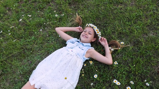 一个可爱的小女孩躺在绿草地上。甘菊。雏菊。孩子笑得很厉害视频素材