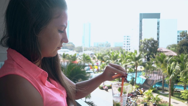 女孩站在酒店的露台上，喝着香甜可口的莫吉托视频素材