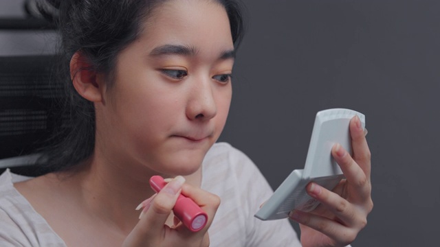 年轻的亚洲影响者女孩在视频中示范如何用美容化妆品化妆。她在家里的客厅里用摄像机录制在线辅导课。社交媒体和直播病毒概念视频下载