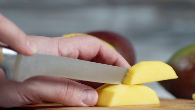 男用手拿着刀在砧板上切着新鲜的芒果。视频下载