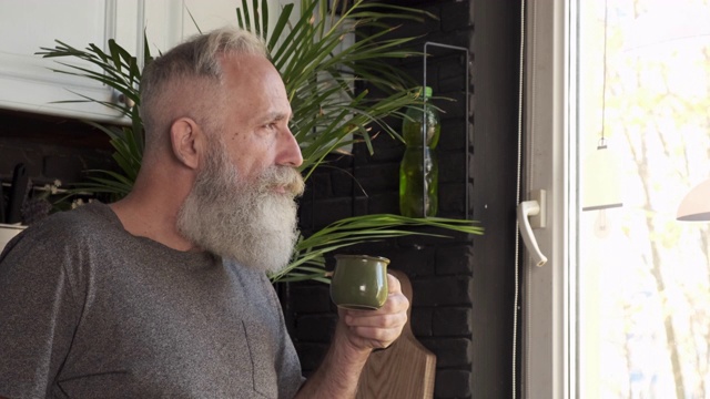 胡子灰白头发的老人在厨房喝茶。特写镜头视频下载