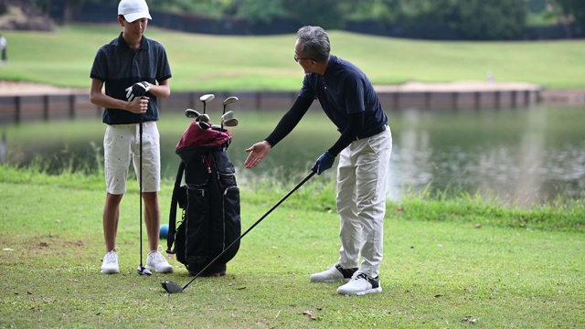 亚洲华人成年人从高尔夫球袋中挑选高尔夫球棒，并在高尔夫球场开球点指导教儿子视频下载