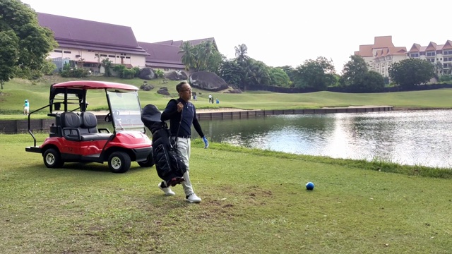 亚洲华人成年男子从高尔夫球车上拿着他的高尔夫球袋走到发球点开始他的高尔夫球比赛视频下载