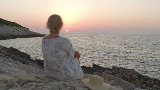 在克罗地亚亚得里亚海宁静的海面上，安详的年轻女子观看日落视频素材