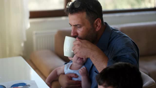 一名男子抱着他刚出生的儿子，在家里用笔记本电脑工作视频素材