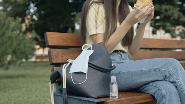 SLO MO保护性面罩挂在钱包前的朋友在公园的长凳上吃汉堡视频素材