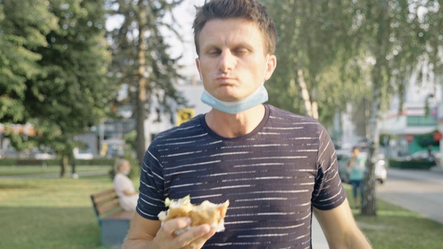 戴着保护面罩的男子在公园里吃汉堡视频素材
