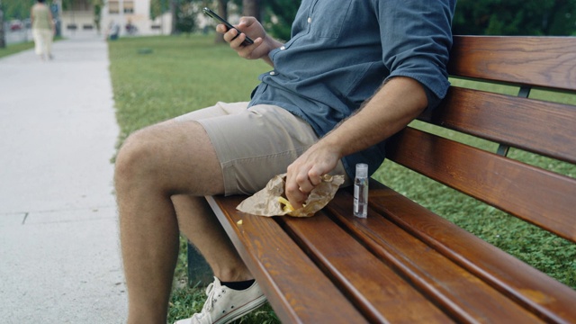 一名戴着保护面罩的年轻人在公园的长椅上滚动手机视频素材