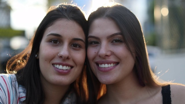 两名年轻的千禧一代女性在外面对着镜头微笑。女友摆姿势与镜头光晕肖像视频素材