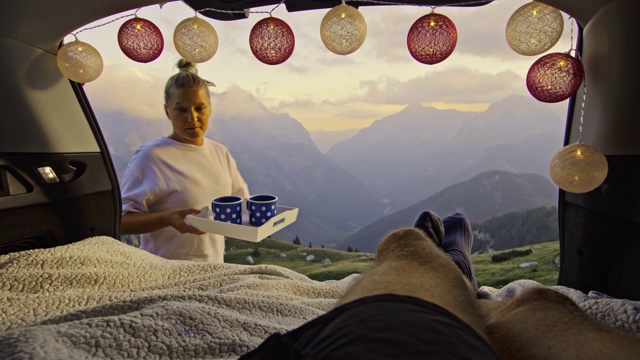 SLO MO女露营者在车里给她的伙伴带咖啡，享受在山上的早晨视频素材