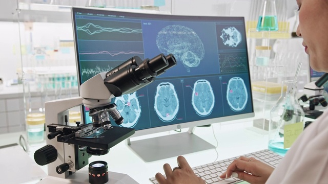 拿着显微镜的女科学家。电脑屏幕上的脑电波扫描研究视频素材
