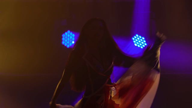 一个女孩的剪影在一个黑暗的工作室与烟雾和蓝色霓虹灯跳舞。迷人的黑发穿着性感的西装在英国国旗的颜色和莱茵石。当代女舞表演视频素材