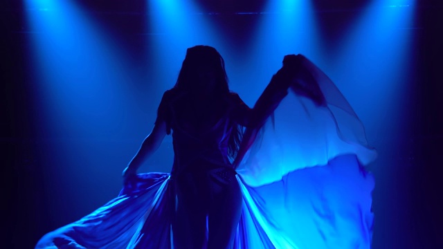 一个女孩的剪影在一个黑暗的工作室与烟雾和蓝色霓虹灯跳舞。迷人的黑发穿着性感的西装在英国国旗的颜色和莱茵石。当代女舞表演视频素材