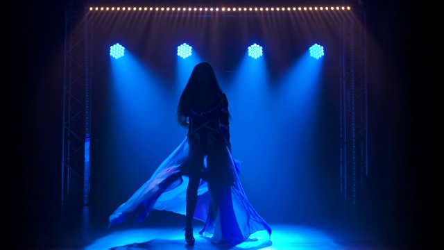 剪影苗条高的女孩在英国国旗和莱茵石的颜色性感的套装跳舞。在黑暗的工作室里用烟雾和蓝色的霓虹灯拍摄视频素材