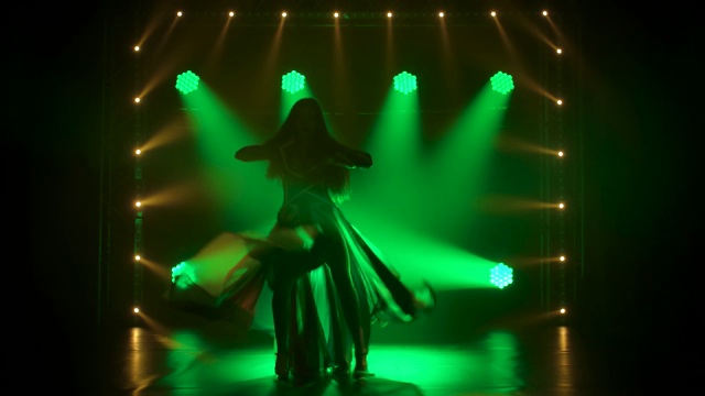 苗条高挑的女人热情地跳舞在黑暗的工作室与烟雾和绿色霓虹灯。剪影迷人的黑发在性感的西装在英国国旗的颜色和莱茵石。慢动作视频下载
