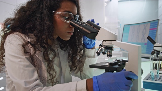 非洲女科学家，拿着显微镜。实验室玻璃器皿在她身后。团队背景视频素材