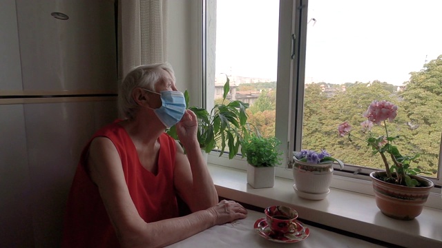 2019冠状病毒病、健康、安全和大流行概念——坐在窗边的孤独老年妇女视频素材